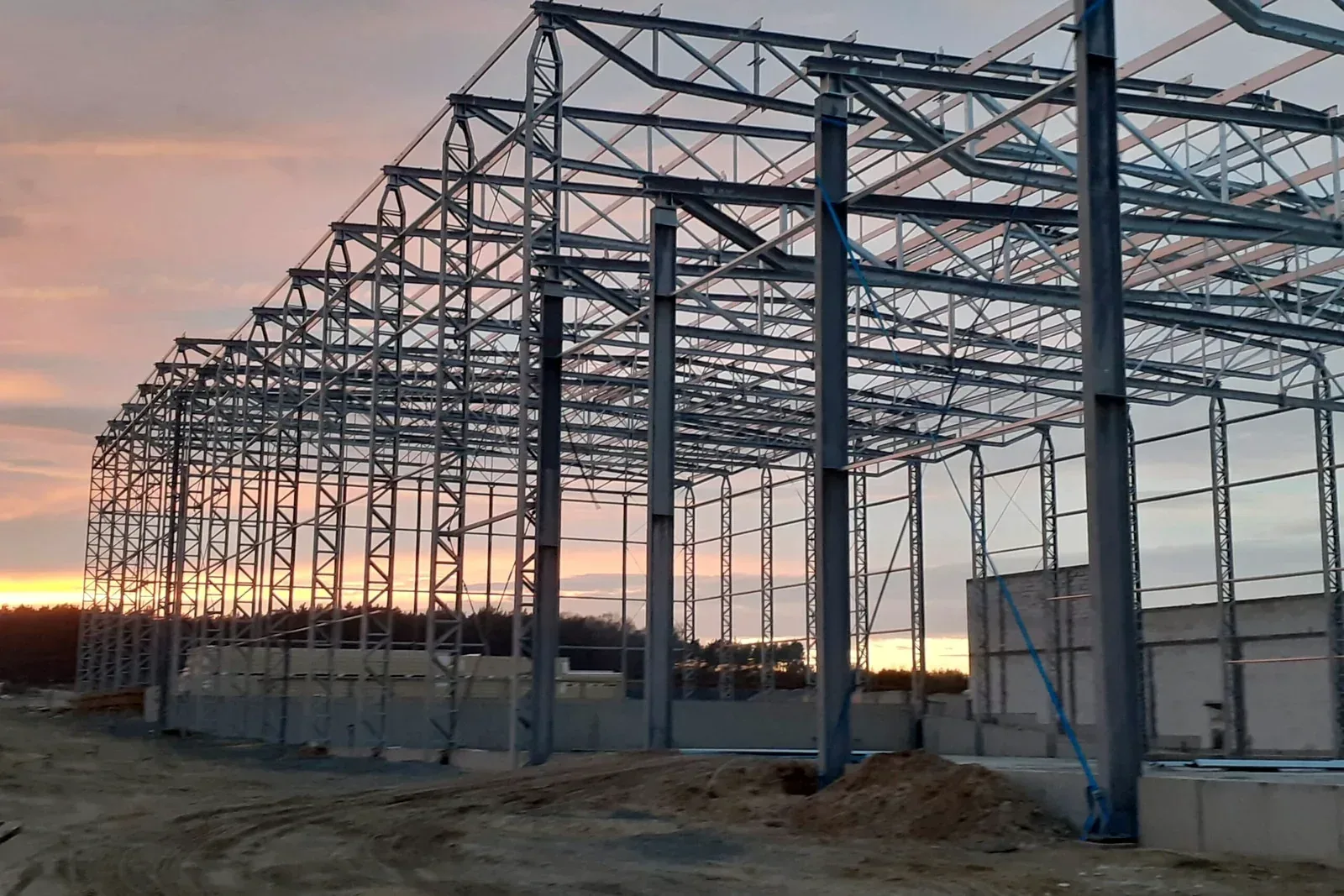 Konstrukcja stalowa magazynu wysokiego składowania w trakcie montażu, zdjęcie o zachodzie słońca